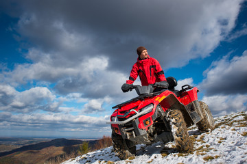 Bottom view of a guy on the sports atv quad bike at the snow-covered slope against the blue cloudy sky on a sunny day in the mountains © anatoliy_gleb
