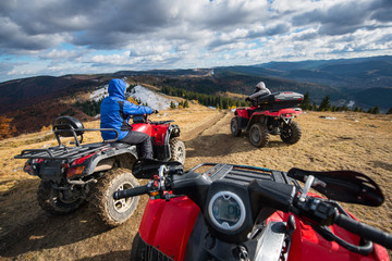 View from a quad bike with men driving an ATV in front on the top of mountain trail with perfect background mountains, forests and sky with cumulus clouds in autumn © anatoliy_gleb