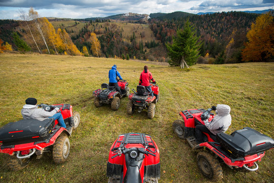 Top view of four men at off-road vehicles prepared to go down the hill. Beautiful landscape of rolling countryside and colorful forest under the sky with cumulus clouds in autumn