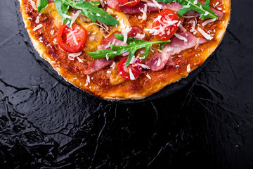 Homemade pizza with prosciutto, tomato, arugula on black slate board. Top view. Copy space.