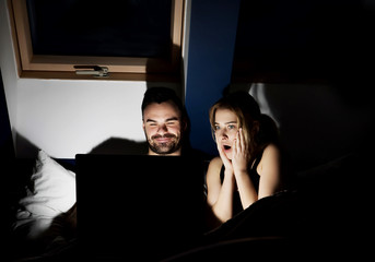 Young couple with laptop watching movie in bed