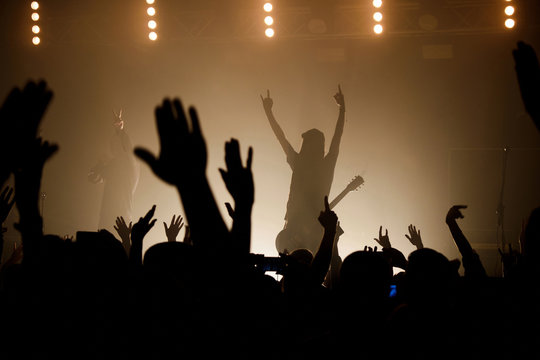 Lit silhouettes of musicians on the smoky stage raising up hand with crowd