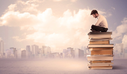 Man sitting on pile of books above city