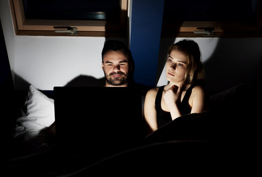 Young couple with laptop watching movie in bed