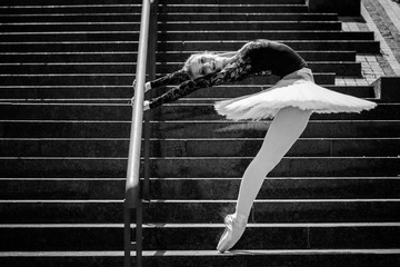 Street dancing ballerina in pointe shoes and white concert tutu at city. Ballerina dancing on the street.Young beautiful ballerina in dress and pointe shoes dancing outdoors. - obrazy, fototapety, plakaty