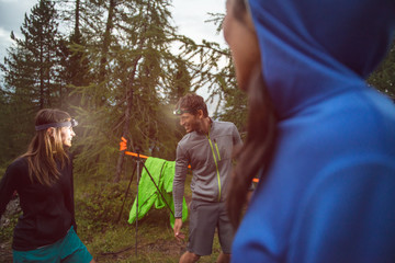 Man and woman joking and smiling with headlamp in evening near camping. Group of friends people...