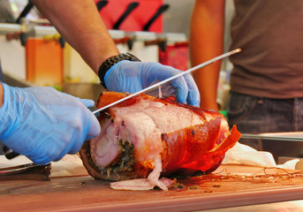Slow-roast rolled pork belly with crispy crackling is sliced by the chef. Lechon porchetta pork roast.