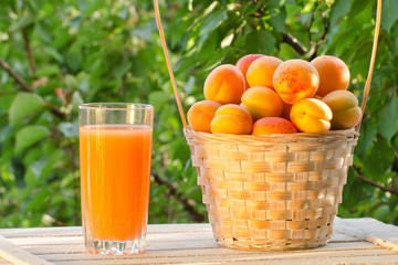Apricots in a wicker basket and a glass of juice on a green background, sunlight