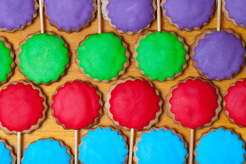 Gingerbread cookies with colored mastic on sticks on the old wooden cutting board