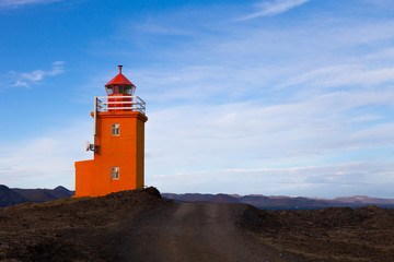 Fototapeta na wymiar Orange lighthouse on a stony coast in Iceland