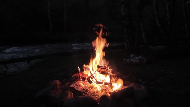Campfire burns brightly at night along the beautiful beach of river