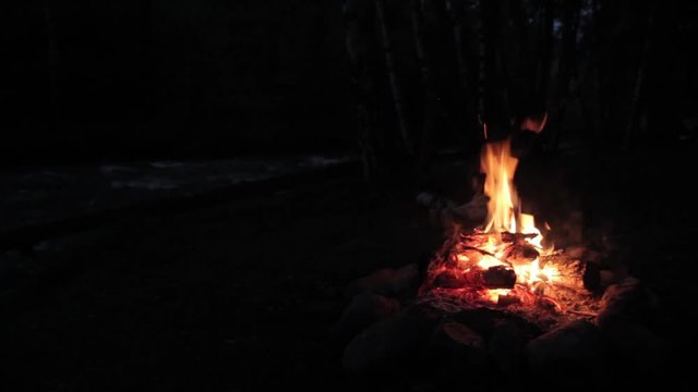 Campfire burns brightly at night along the beautiful beach of river