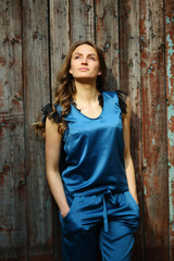 Fototapeta premium Beautiful young woman in silk clothes, looking up, inspired, outdoor, daytime, wavy hair, street style, wooden ancient wall, hands in pockets