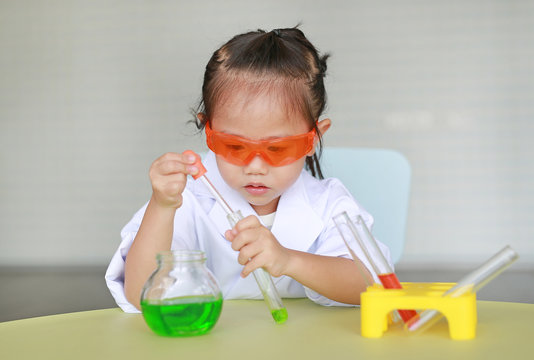 Child in scientist uniform holding test tube with liquid.