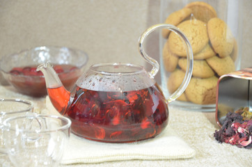 Serving table for breakfast, red tea in teapot. tea leaves, hibiscus and two glass cups for tea