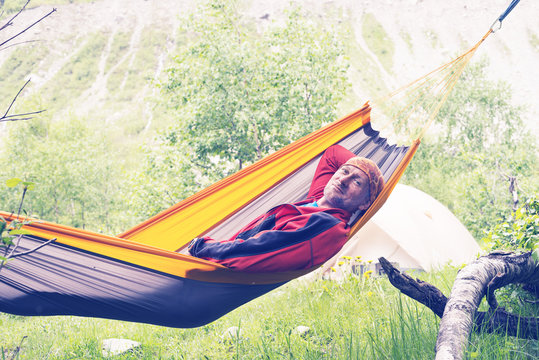 Happy hiker is relaxing in hammock on the alpine meadow
