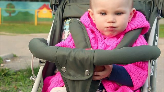 Baby girl sits in a baby stroller and eats an apple