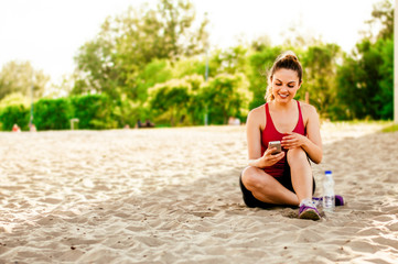 Fototapeta na wymiar Girl sits on sand and enjoys the phone