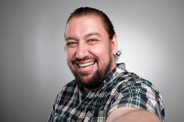 Obraz premium Beautiful young man in casual clothes make selfie on a gray background. He has a happy face, smiling with teeth.