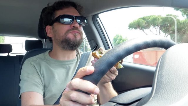Man eating hamburger while driving car closeup