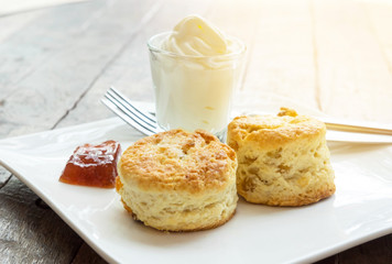 Scones with cream and jam in white plate on wooden desk