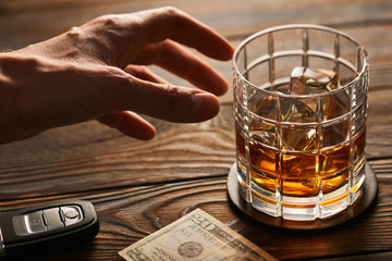 Man's hand reaching to glass with alcohol drink and car key. Drink and drive concept.