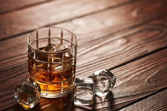 Glass of whiskey with ice cubes on wooden table