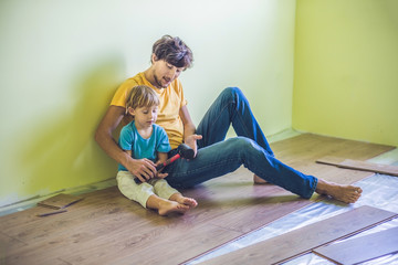 Father and son installing new wooden laminate flooring. infrared floor heating system under...