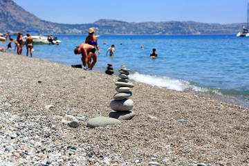 Stos płaskich kamieni na kamienistej plaży, ludzie, plażowicze, Rodos, Grecja.