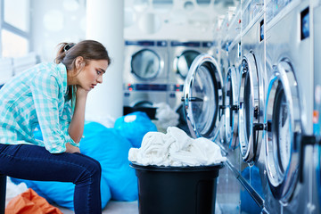 Bored woman sitting opposite to washing machines
