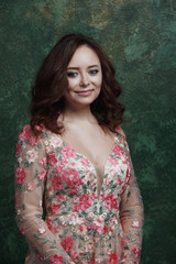 Beautiful young woman in a chic floral dress. Girl posing on a green background.