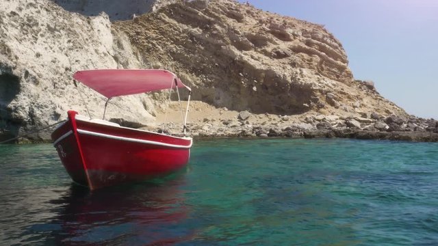 Red boat docked on an Island in front of a cave