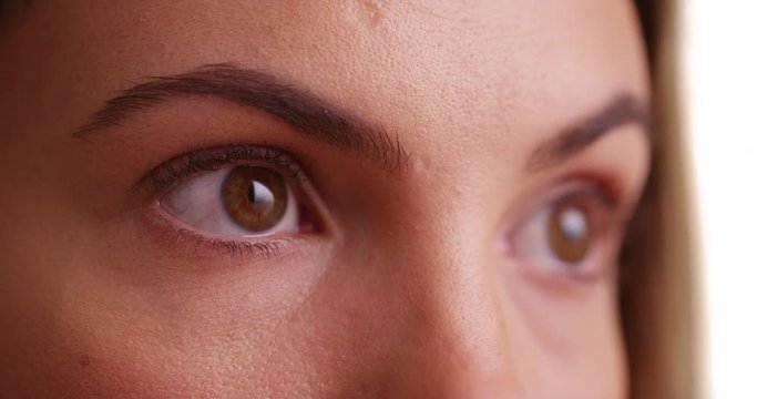 Close up of female millennial's eyes blinking on white background. Close-up of young woman's brown eyes looking off camera in studio. 4k 