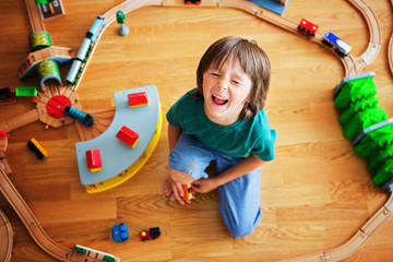 Sweet preschool child, playing with wooden railway and trains at home