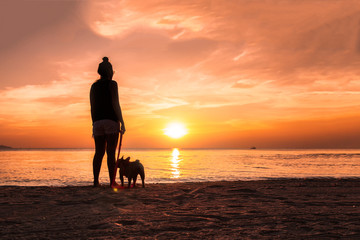 Woman with her dog in the beach on golden sunset background. 