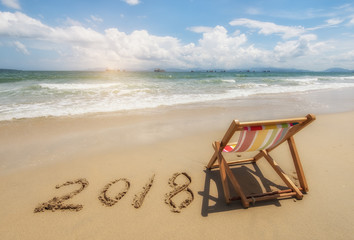 Fototapeta na wymiar Deck chair with 2018 written in sand write on tropical beach.