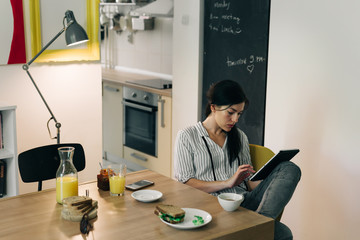 Online leisure time.young woman having breakfast while working on her tablet at home