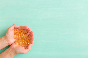 Top view on woman's hands holding pile of capsules Omega 3 on turquoise background. - obrazy, fototapety, plakaty