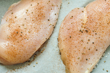 Uncooked chicken breasts with sea salt and black pepper on baking paper. Raw chicken fillet. Healthy cooking concept