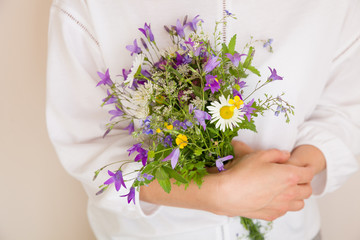 Closeup of woman's hands holding beautiful bunch of wild flowers. Girl with summer bouquet at white wall