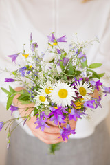 Closeup of woman's hands holding beautiful bunch of wild flowers. Girl with summer bouquet at white wall