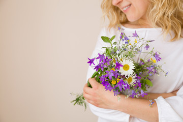 Closeup of woman's hands holding beautiful bunch of wild flowers. Girl with summer bouquet at white wall