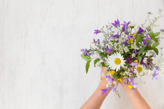 Beautiful bunch of wild flowers in woman's hands on the white wooden background. Flowers from the park. Summer. Gift bouquet.