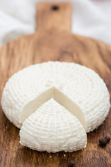 Sliced round white homemade cheese - traditional milk creamy dairy product on vintage wooden board. Rustic style.
