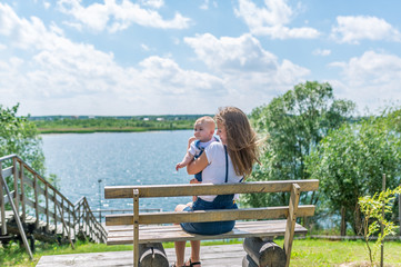 Fototapeta premium Young mother with infant sitting on the bench near a river