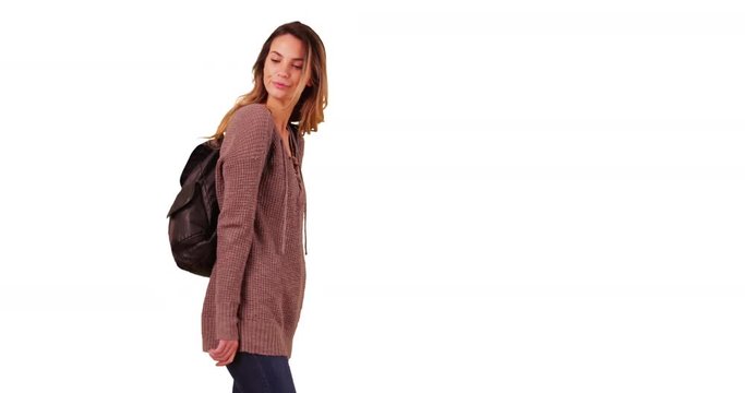Attractive female millennial with backpack waiting for someone on white background with copyspace. Young white woman or student in her 20s standing with hands in pockets in studio with copy space. 4k 
