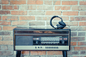 Old vintage antique radio with headphones on red brick wall background. Toned image. Copy space.