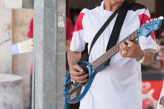 Crop Old Asian man playing guitar made of tennis racket To raise money to help poor people in public.