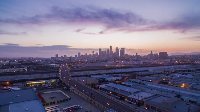 Aerial timelapse in motion (hyperlapse) at sunset facing downtown Los Angeles at twilight with the sky changing from day to night with pink skies and clouds above and traffic on a busy street