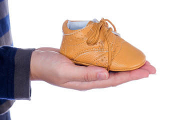 Children's shoes on women's hand on wooden background.